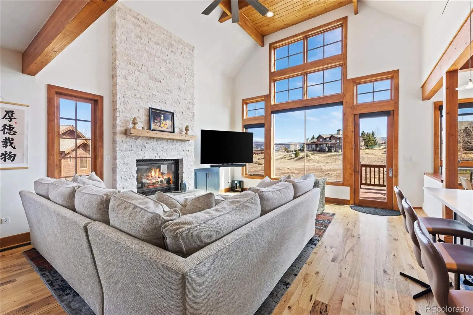 Great room with vaulted timber-beam ceiling, stone fireplace and tall windows